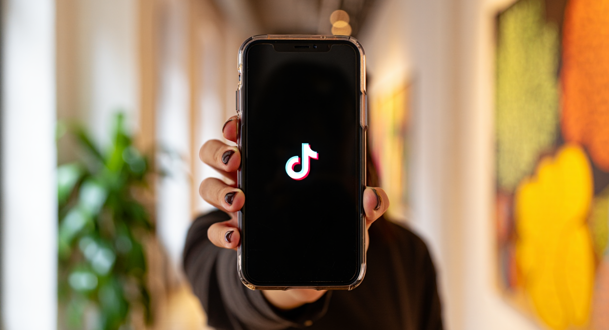 Dame hält ein Smartphone mit TikTok Logo am Bildschirm in die Kamera. 